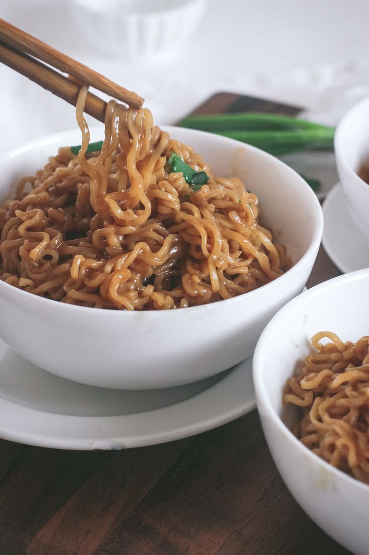 two white bowls filled with noodles and chopsticks