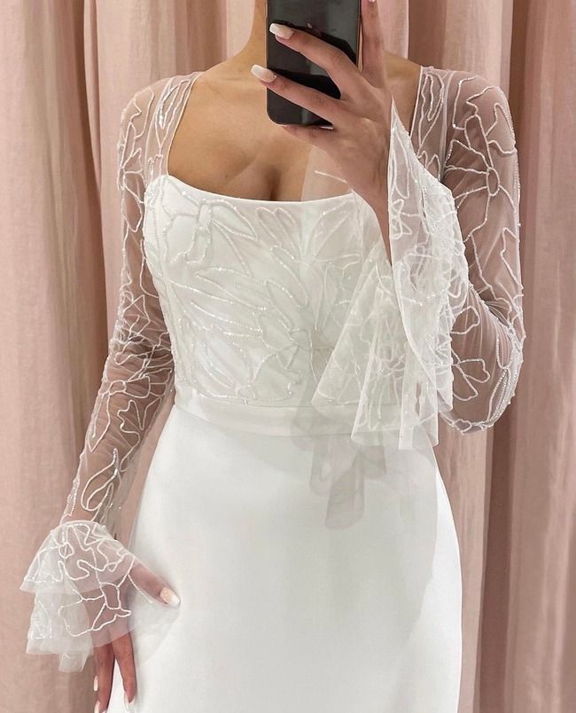 a woman taking a selfie in front of a mirror wearing a white dress with sheer sleeves