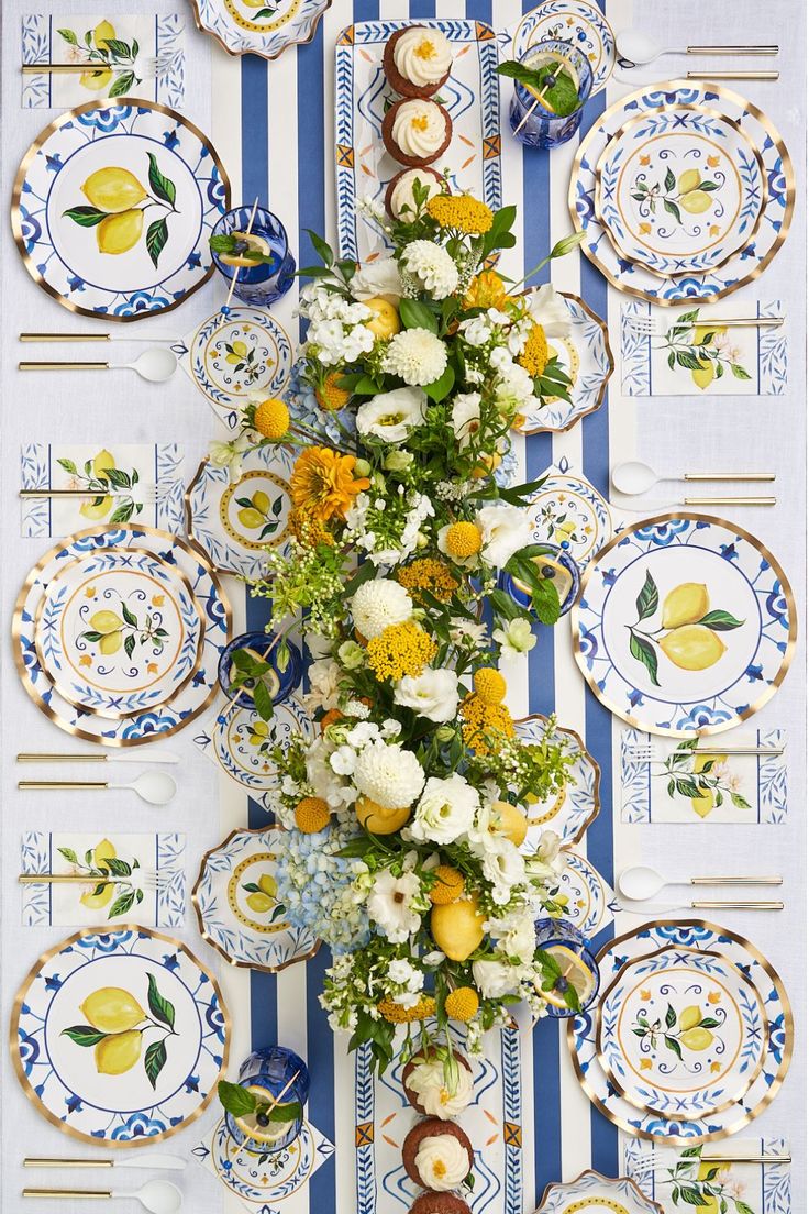 an arrangement of flowers and plates on a table with blue and white striped wallpaper