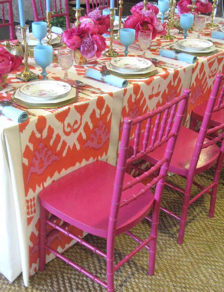 the table is set with pink chairs and plates