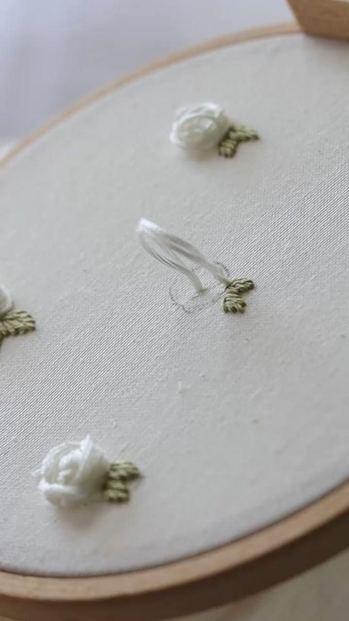 the embroidery is being worked on with white thread and green flower decorations are placed next to each other