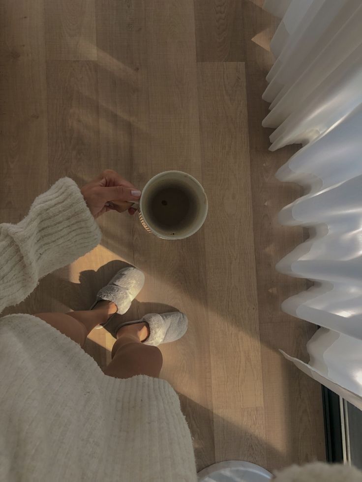 a person holding a coffee cup in their hand while standing on the floor next to a window