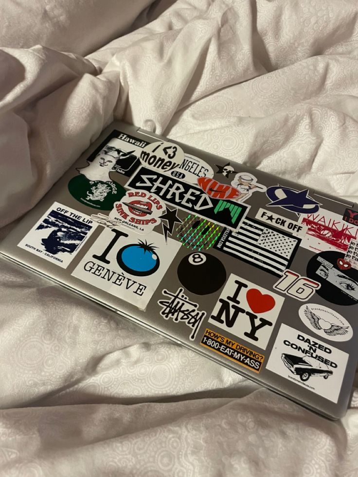 a laptop covered in stickers on top of a bed