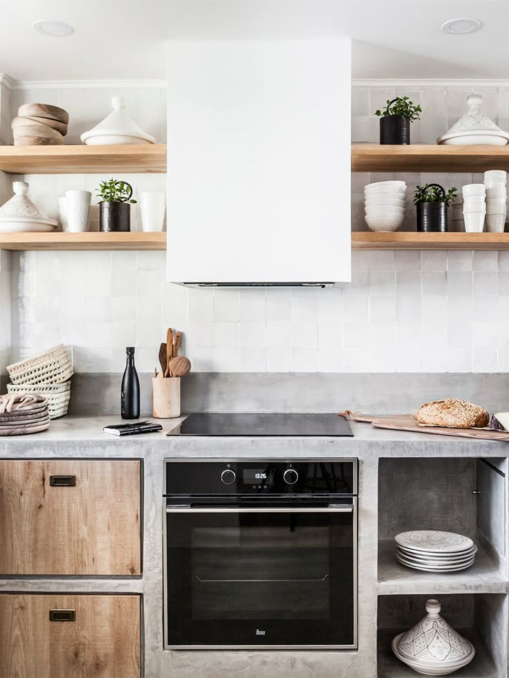 a stove top oven sitting inside of a kitchen next to wooden cabinets and open shelves