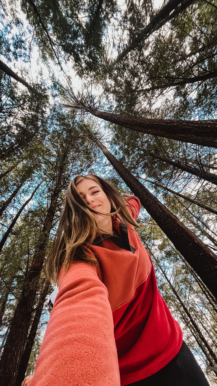 a woman standing in front of tall trees looking up at the sky