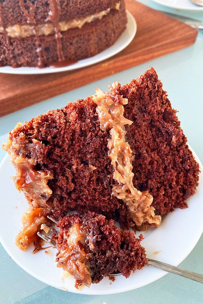 a slice of chocolate cake on a white plate with caramel icing and pecans