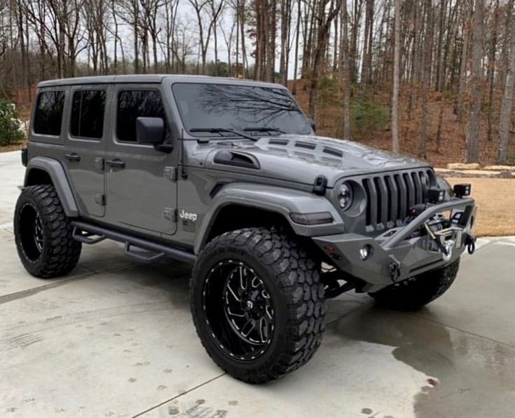 a gray jeep is parked in front of some trees