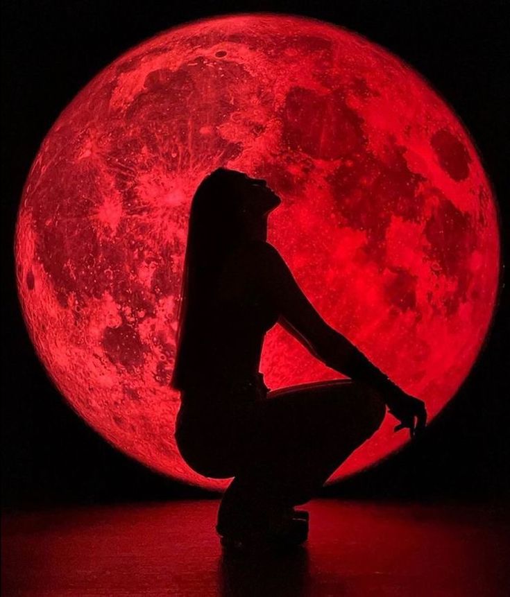 a woman kneeling in front of a red full moon