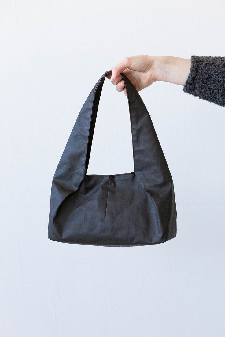 a hand holding a black leather bag in front of a white wall with the bottom half open