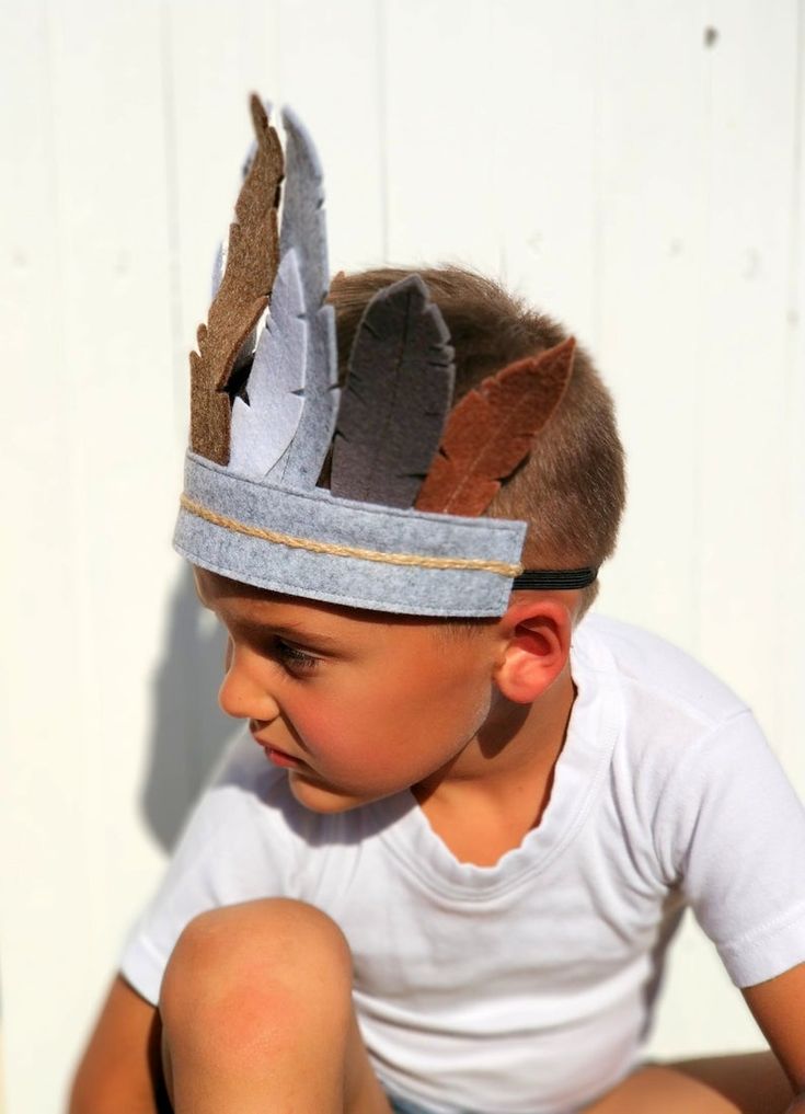 a young boy wearing a hat with feathers on it's head sitting against a white wall