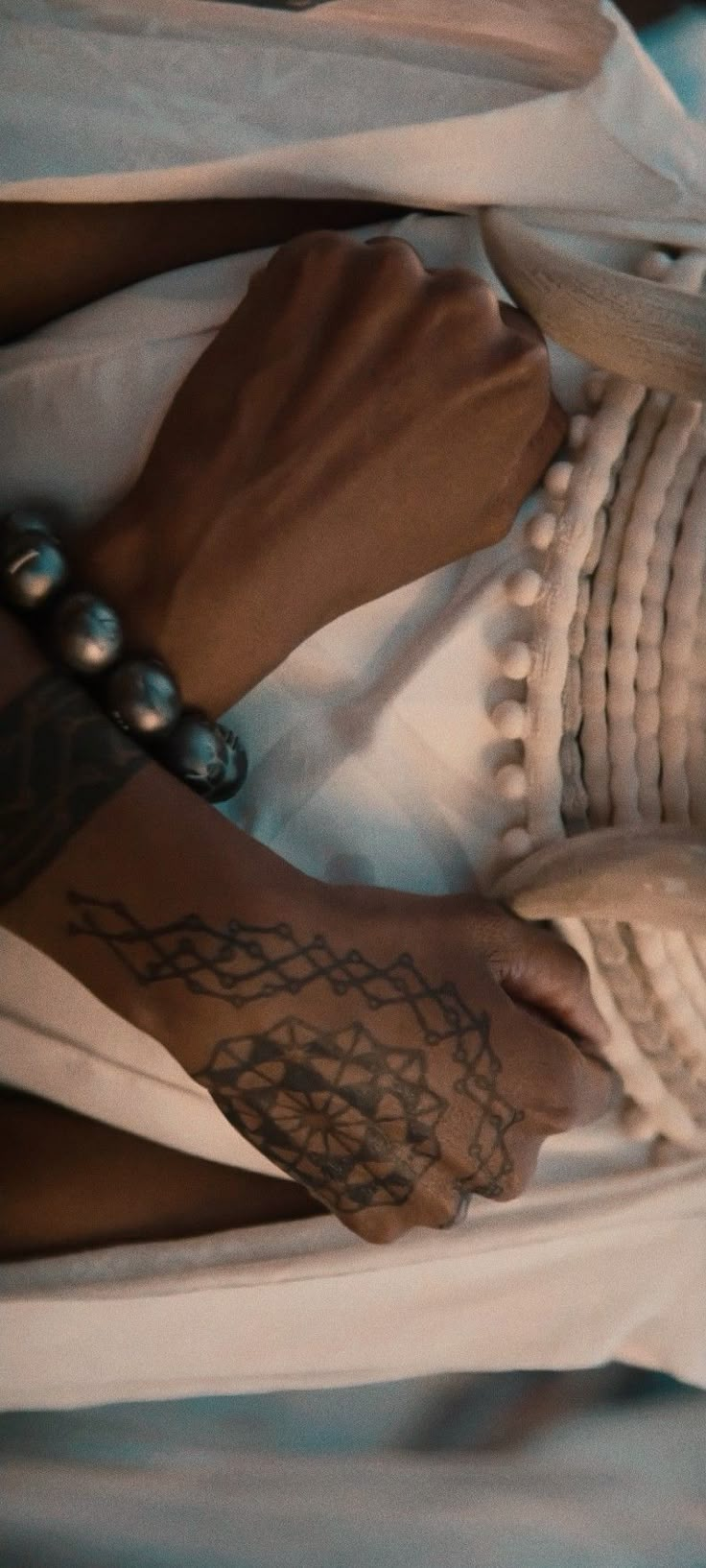 a woman's hand with tattoos on her left arm and right foot resting on a bed