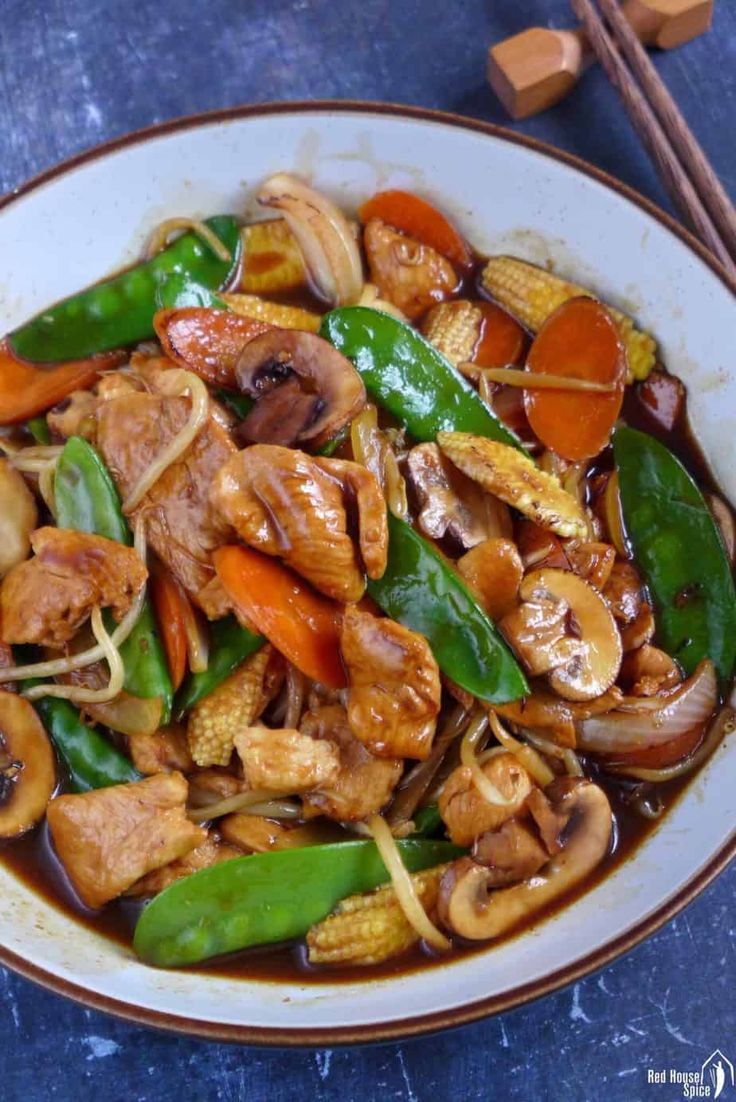 a white bowl filled with stir fry vegetables and meat on top of a blue table