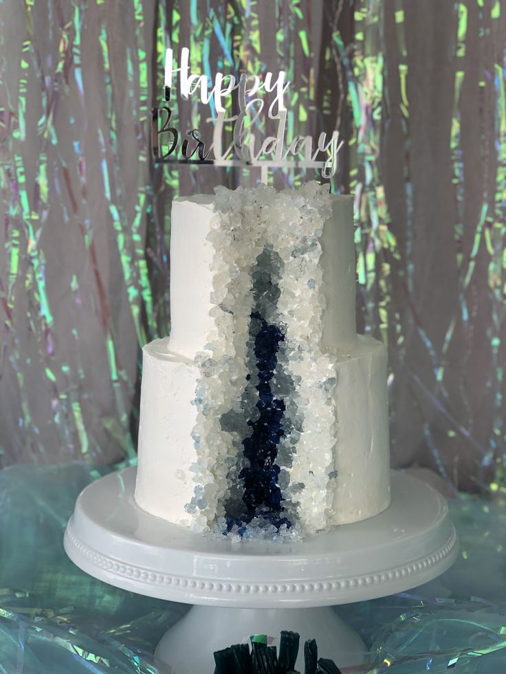 a white cake with blue and green frosting sitting on top of a table in front of a backdrop