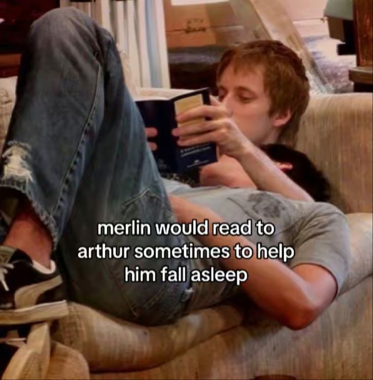 a man laying on top of a couch reading a book with his feet up in the air