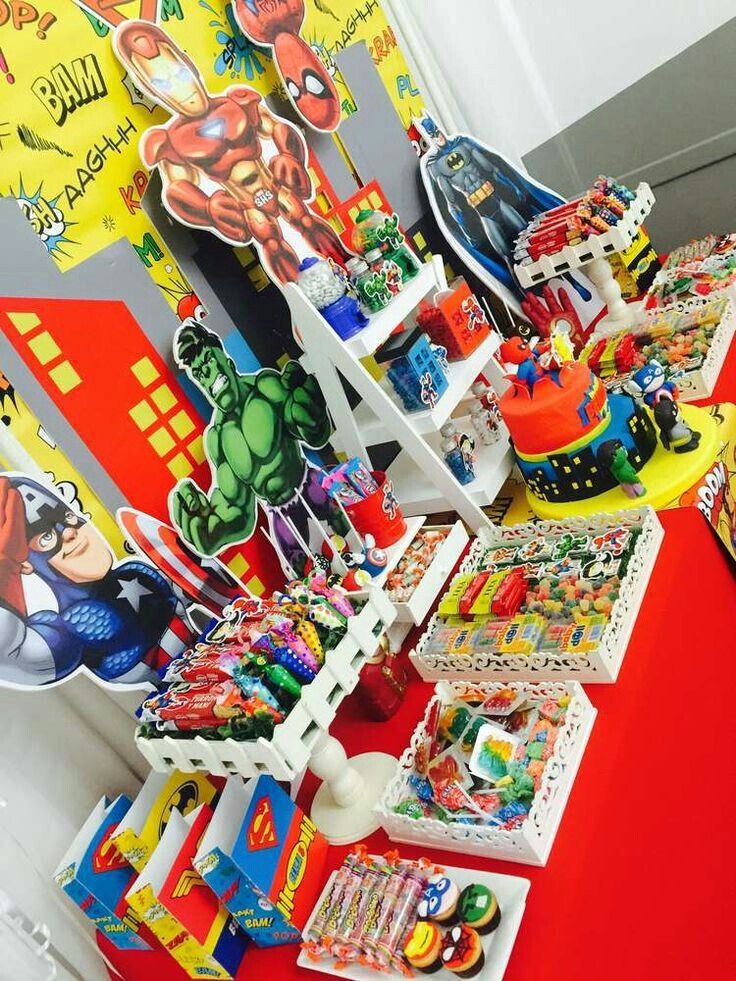 a red table topped with lots of candy and decorations next to a wall covered in comic books