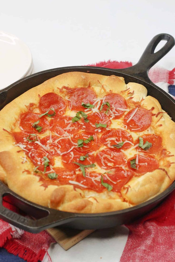 a pepperoni pizza in a cast iron skillet on a red, white and blue table cloth