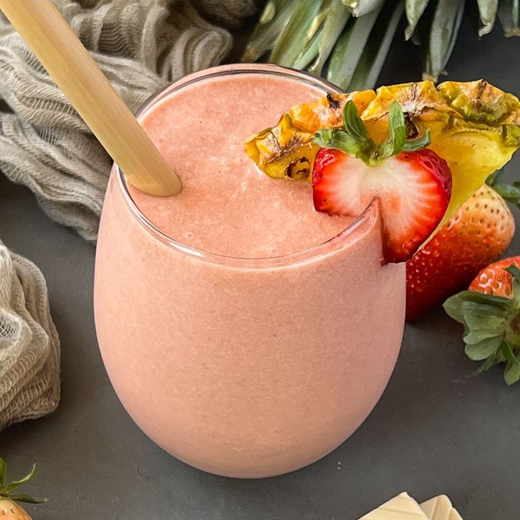 a smoothie in a glass with strawberries on the side