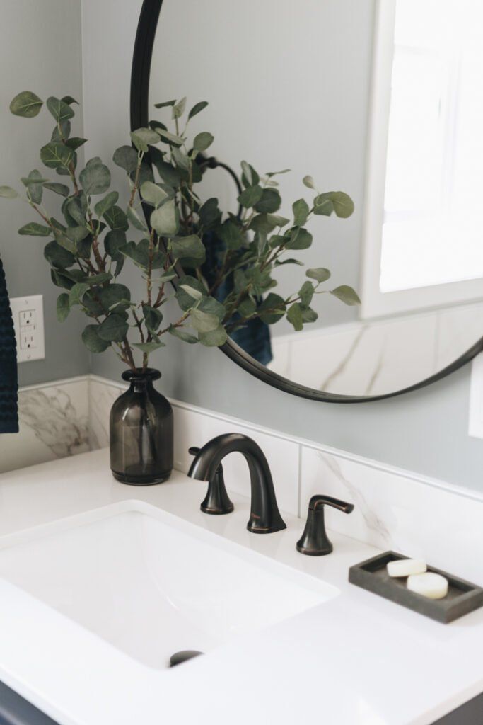 a white sink sitting under a mirror next to a black faucet and a plant