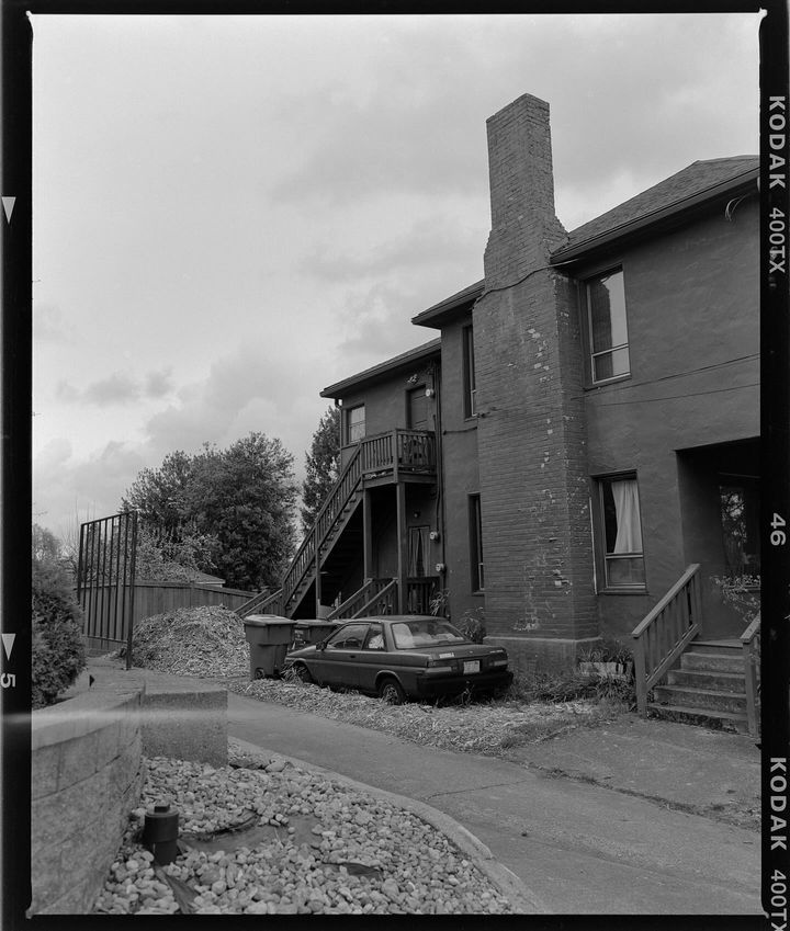 black and white photograph of an old house with a car parked in the front yard