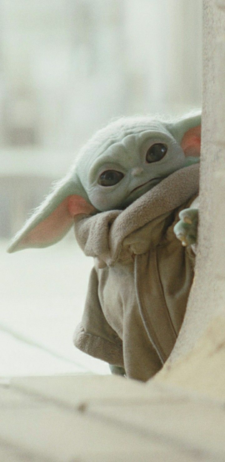 a baby yoda doll is peeking out from behind a wall and looking at the camera