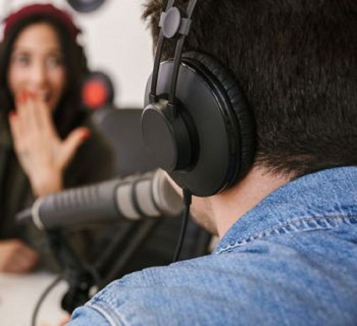 a man with headphones on sitting in front of a microphone talking to a woman