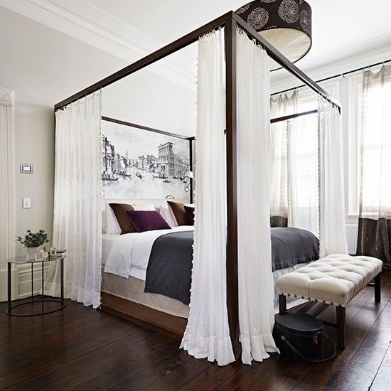 a four poster bed with white drapes on the top and purple pillows on the bottom