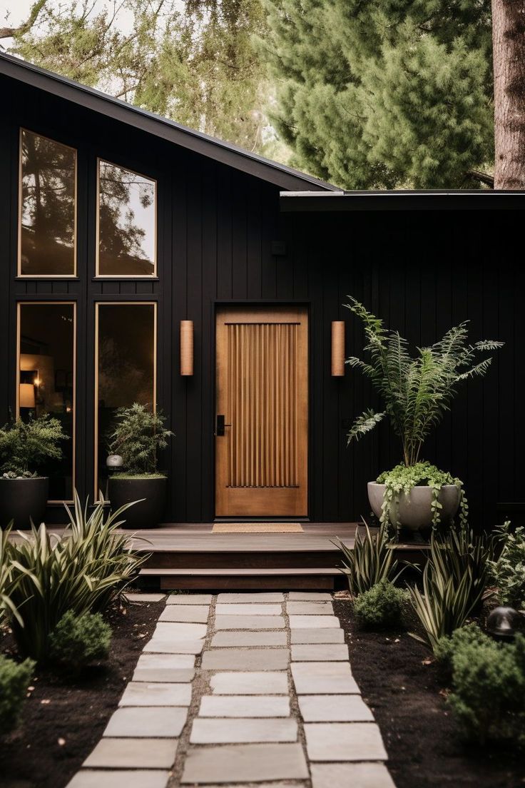 a black house with lots of windows and plants on the front lawn, along with steps leading up to it