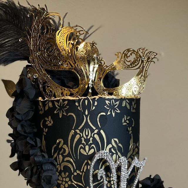 a black and gold masquerade cake decorated with feathers, jewels, and beads