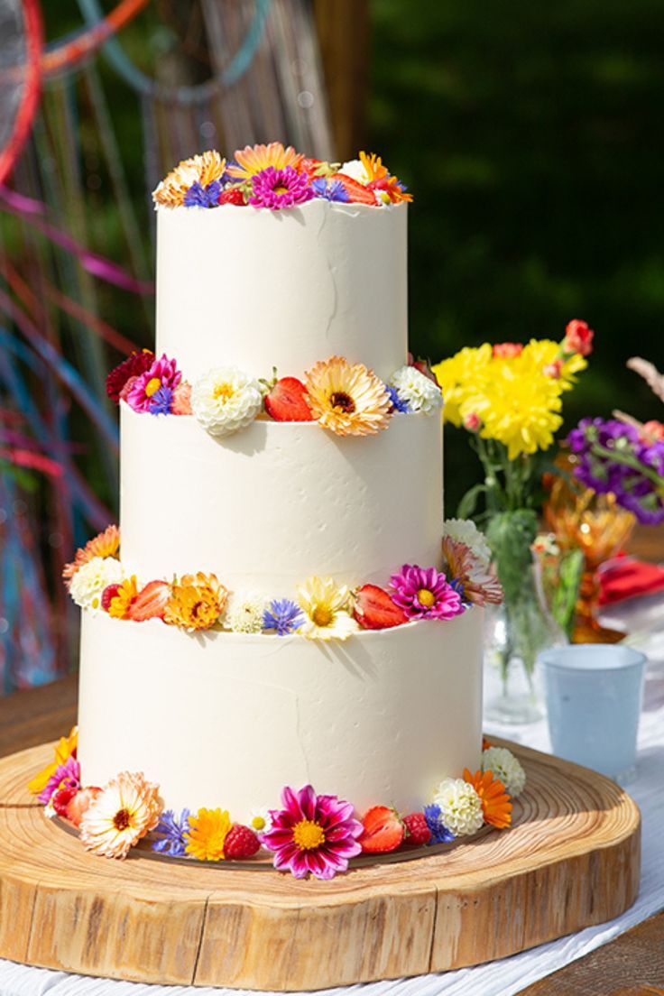 a three tiered cake on a wooden table with colorful flowers and streamers in the background