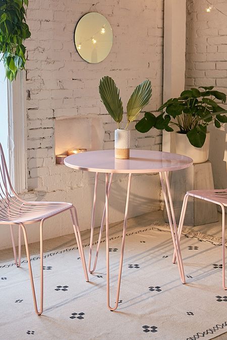 two pink chairs and a table in a room with plants on the wall behind them