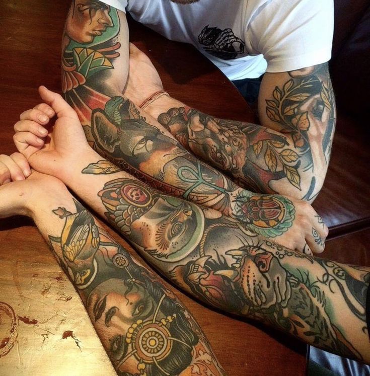 two men with tattoos on their arms sitting next to each other at a wooden table