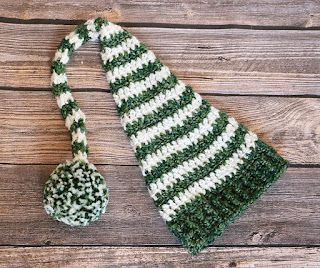 a green and white crocheted hat on top of a wooden table next to a spoon