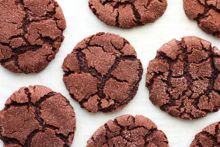 several chocolate cookies that have been cracked and are sitting on a white tablecloth with other cookies in the background