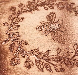 a close up of a bee on a piece of wood with flowers and leaves around it