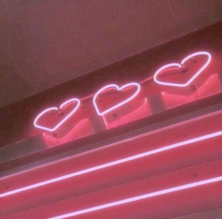 three heart shaped neon signs on the side of a building with red lights above them