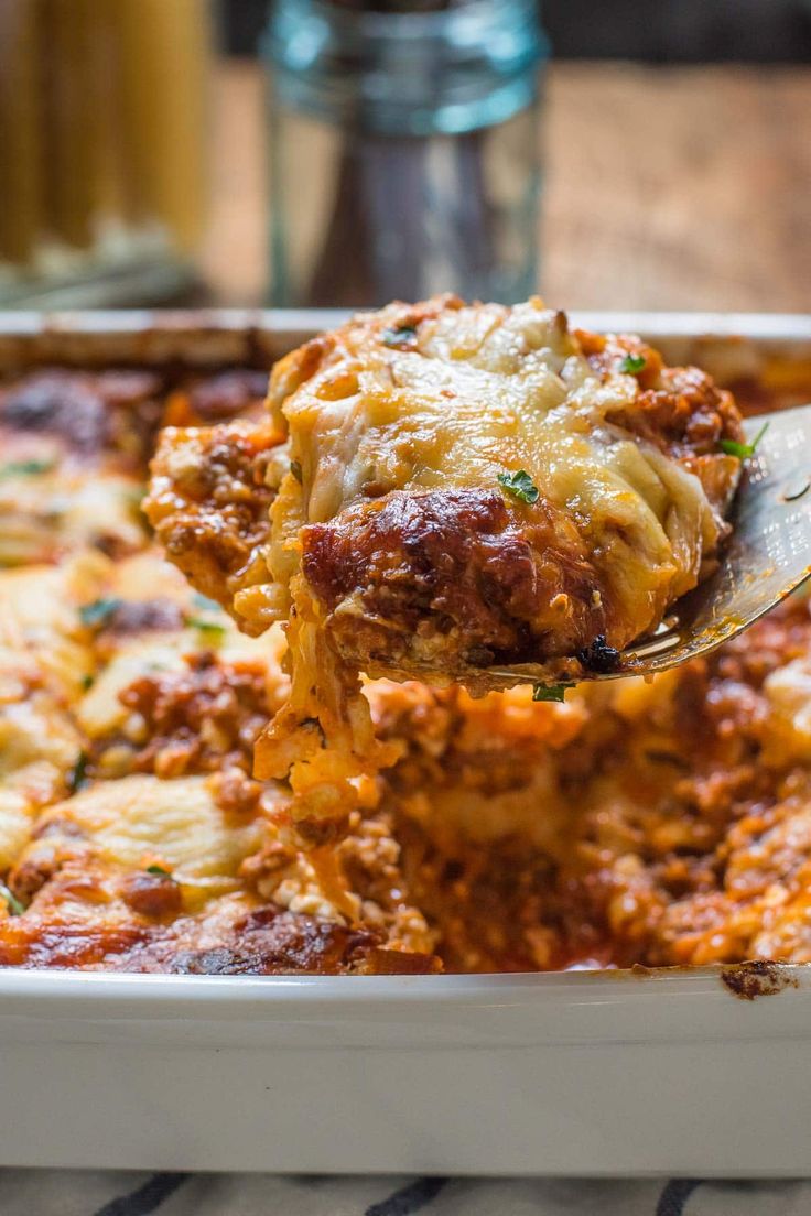 a spoon full of lasagna casserole being lifted from a white dish