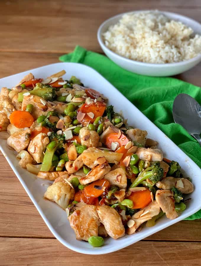 a white plate topped with chicken and veggies next to a bowl of rice