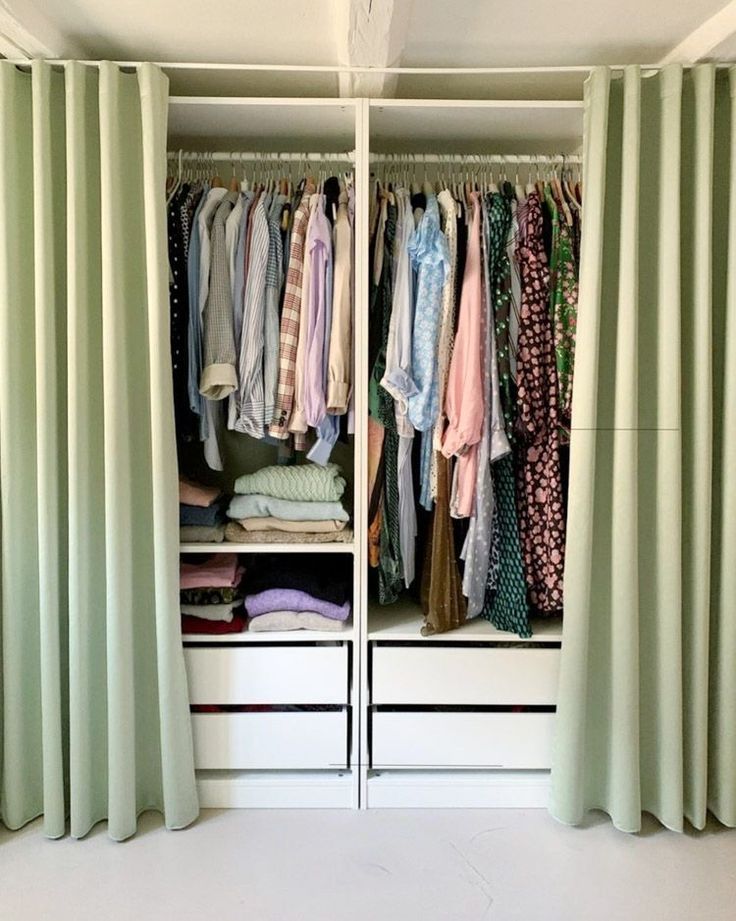 an open closet with clothes hanging on the walls and green drapes covering the doors