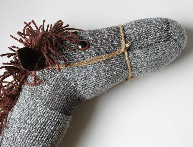 a gray sock with brown fringes and a button on the side is sitting on a white surface