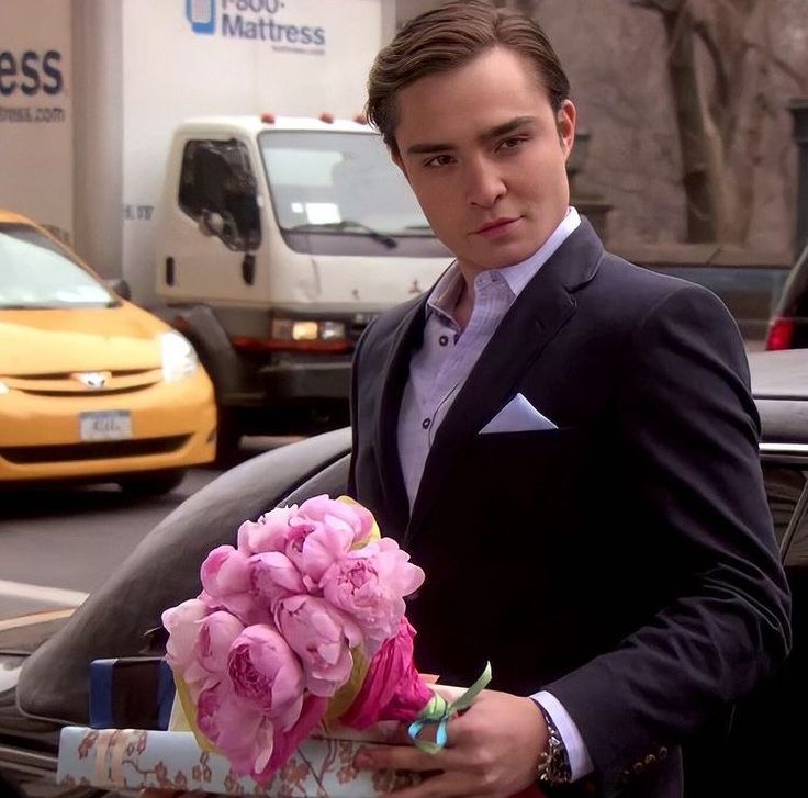 a man in a tuxedo holding a bouquet of pink flowers on the street