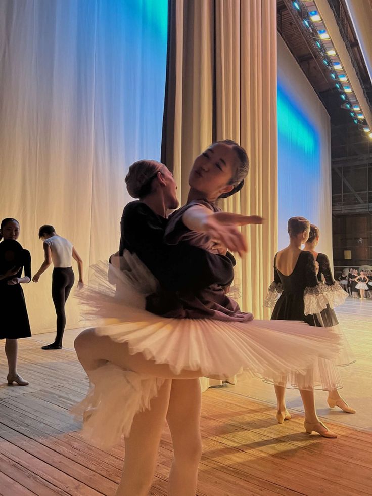 two dancers in tutu skirts are dancing on the stage with other dancers behind them