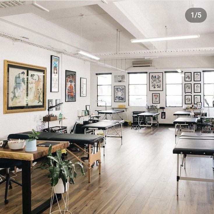 an empty room with tables, chairs and pictures hanging on the wall above them in front of windows