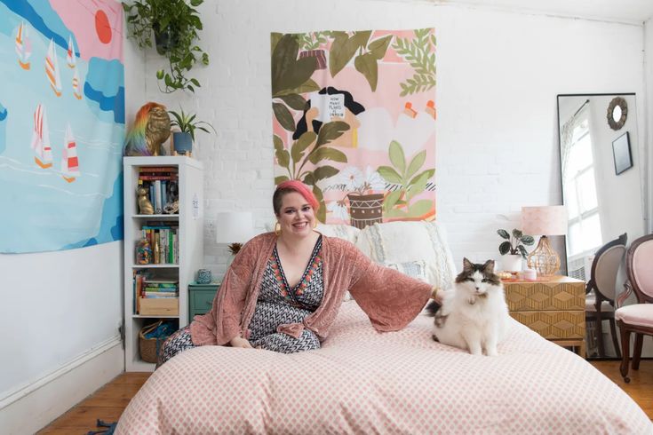 a woman sitting on top of a bed next to a white and black cat in a bedroom