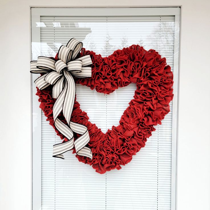 a heart shaped wreath hanging on the side of a window with blinds in front of it