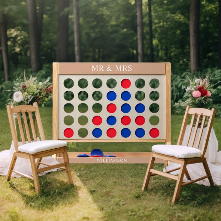 a giant board game set up in the grass with two wooden chairs next to it