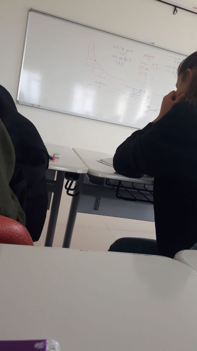 two people sitting at desks in front of a whiteboard