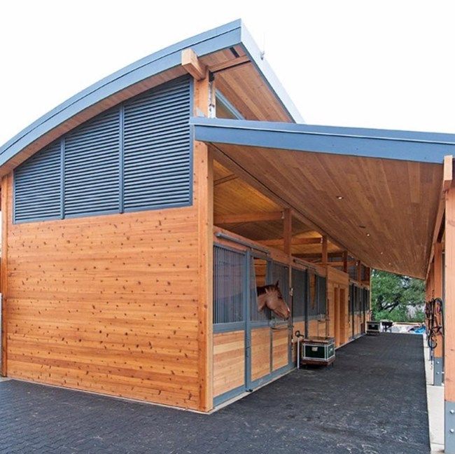 a horse stable with wooden walls and windows on the roof, along with an awning for shade