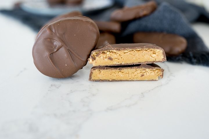 two pieces of chocolate and peanut butter on a marble counter top with cookies in the background