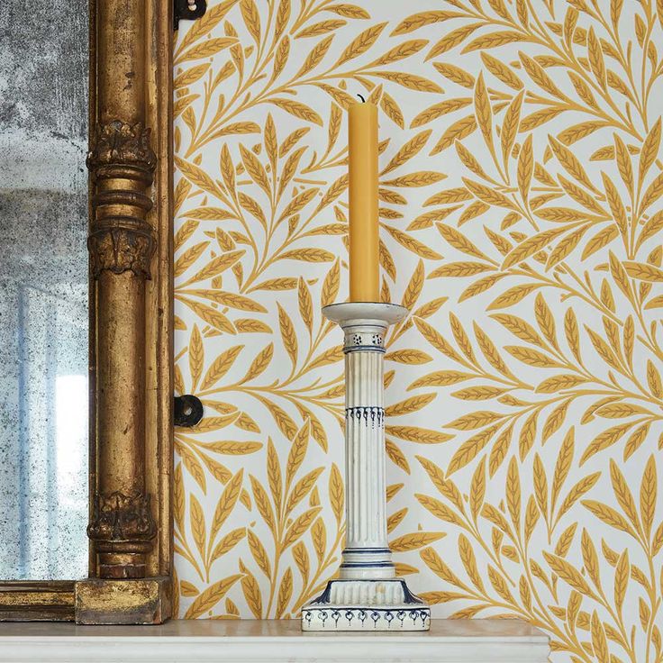 a candle is sitting on top of a mantle in front of a wallpapered mirror