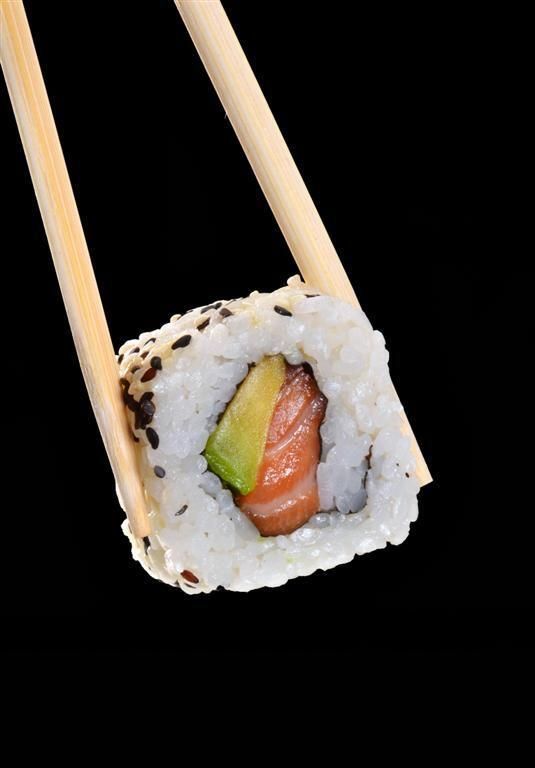 two chopsticks with sushi on them are seen against a black back ground